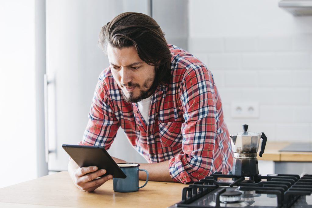 homme qui regarde sa tablette pour voir le prix du gaz avec une plaque de gaz